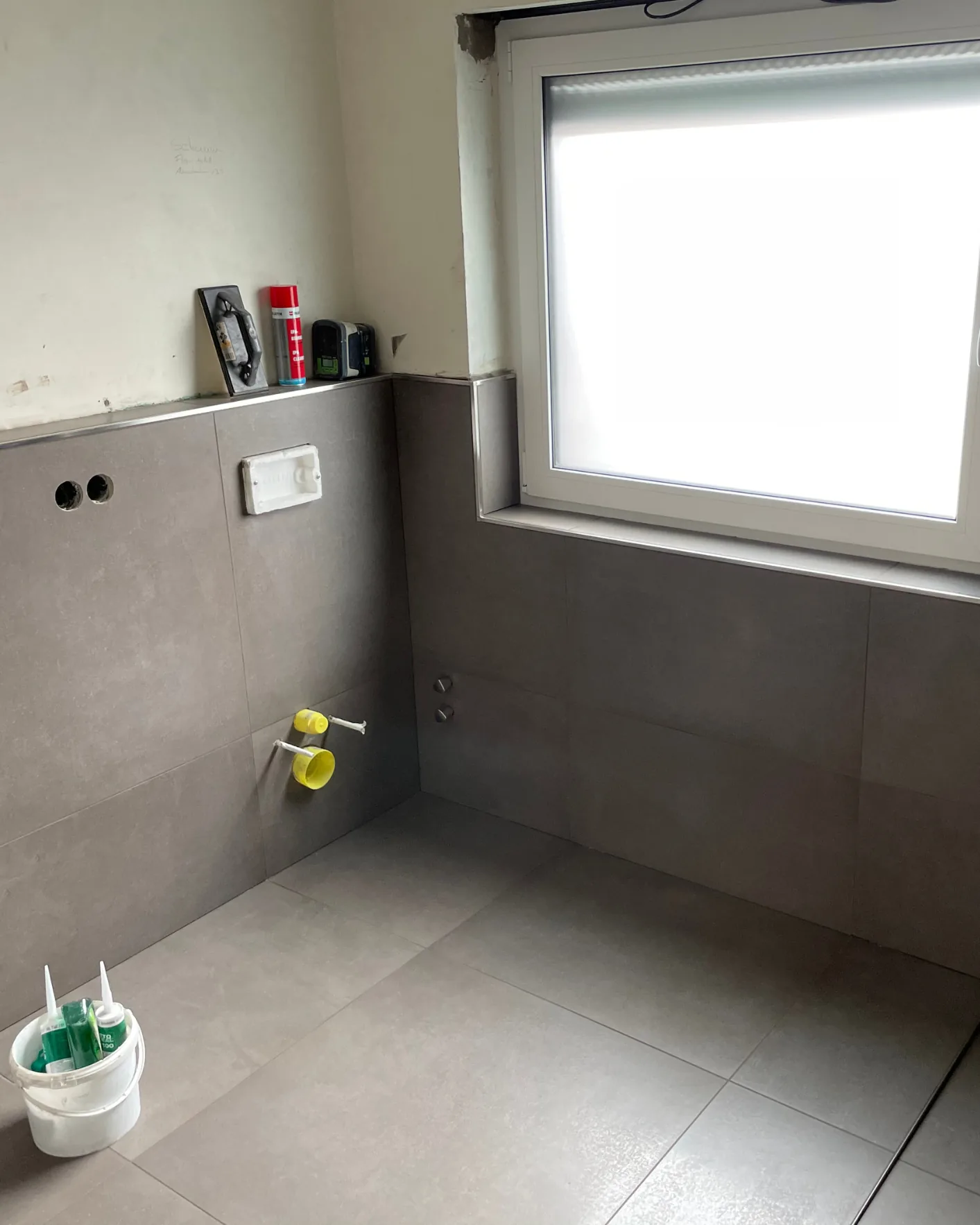 Badezimmer mit grauen Wand- und Bodenfliesen vor der Montage